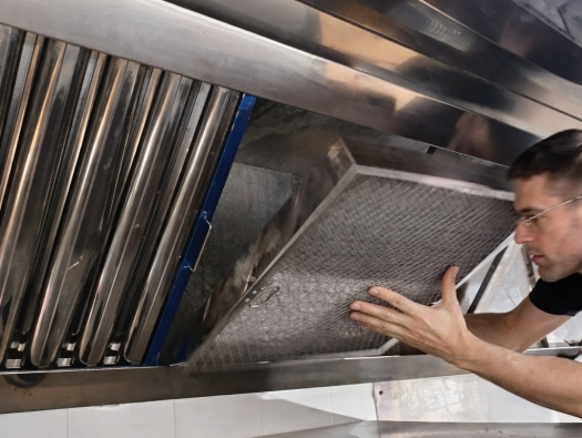 Operario realizando la limpieza de filtros de campanas extractoras industriales retirando filtro de malla metálica